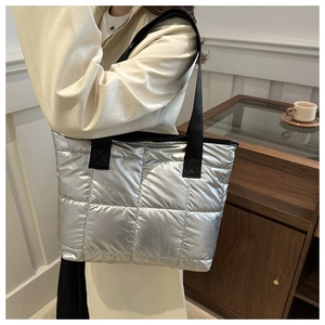 Gros plan du sac cabas matelassé argenté avec bandoulière noire porté par un mannequin en intérieur