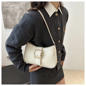 Detailed close-up of a minimalist cream shoulder bag featuring a large gold square buckle