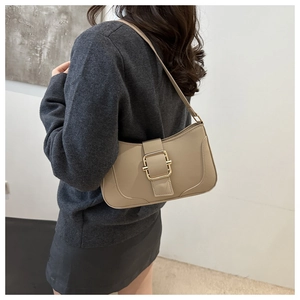 Detail of a beige crescent hobo bag with gold buckle on shoulder of a model