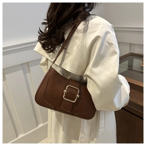 Close-up of a brown leather baguette bag with a gold buckle worn with a trench coat
