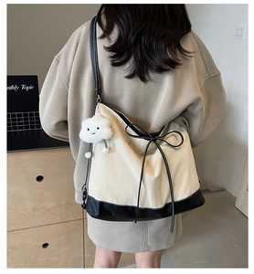 Detail of cream canvas tote bag with black contrast trim, bow accent and plush charm