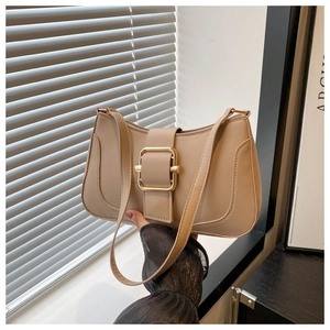 Close-up of minimalist beige shoulder bag featuring a large square gold metal buckle clasp