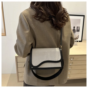 Detail of canvas and black leather crossbody bag with unique wavy flap and gold hardware
