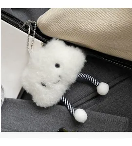 Detail of a white plush cloud charm with striped legs hanging on a canvas bag strap