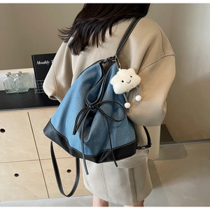Detail of denim tote bag with white cloud plush charm and leather straps in a home setting