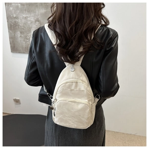 Detail shot of a cream white mini backpack with multi-zipper pockets and pleated texture