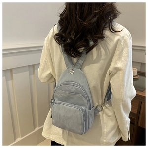 Detail shot of a light blue nylon backpack with multiple zippers on female model