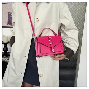 Détail du sac à bandoulière rose avec fermoir doré en V sur un manteau beige