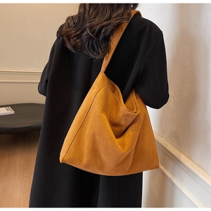 Détail d'un grand sac hobo en daim orange gingembre porté sur un manteau noir élégant