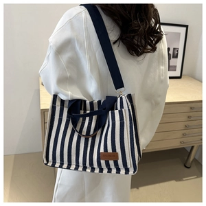 Rear view of striped canvas tote bag with leather fashion tag and navy blue strap