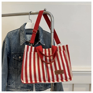 Detail of red and white striped canvas tote bag with brown leather label and wide strap