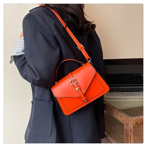 Détail du sac à main orange avec boucles dorées porté par un mannequin dans un bureau