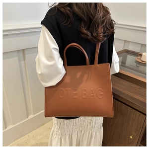 Detail of tan tote bag with embossed text showing dual handles and long shoulder strap