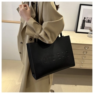 Detail of black leather tote bag featuring embossed TOTE BAG text on a shoulder strap