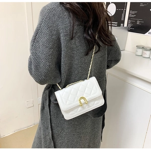 Detail of white quilted crossbody bag with gold horseshoe buckle on a knit cardigan