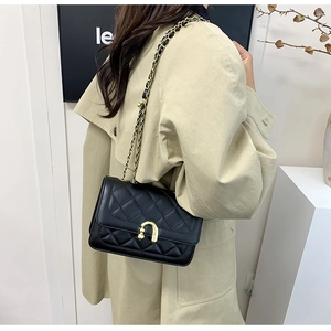 Detailed view of black quilted crossbody bag with gold U-shaped lock on beige trench coat