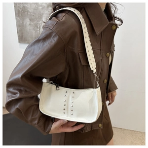 Détail d'un sac à bandoulière en cuir blanc avec rivets argentés sur un blouson moto