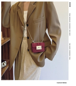 Detail of burgundy mini suede chain bag with gold buckle on brown oversized blazer