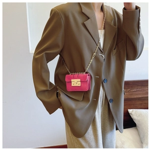 Detailed view of magenta suede mini bag with gold chain and metal lock on olive blazer