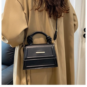 Detail of black stylish handbag featuring a unique knotted handle and gold metal bar accent