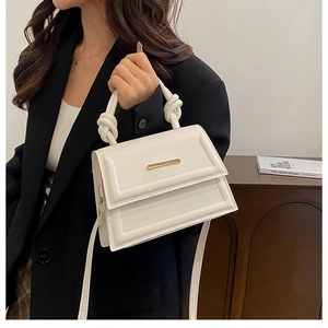 Close-up of white PU leather square handbag featuring a top handle knot and gold bar detail