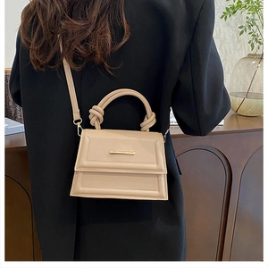 Detail of apricot crossbody bag with knotted handle and elegant gold metal trim on flap