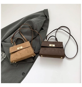 Détail de sacs bandoulière en daim camel et marron avec fermoirs sur un blazer gris