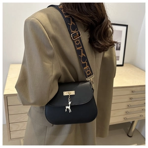 Detail of black PU leather saddle bag featuring deer pendant and wide graphic strap