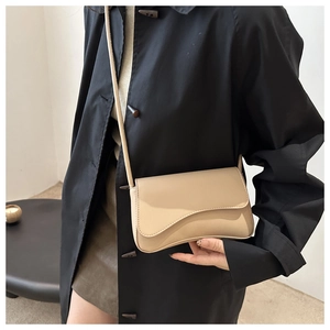 Detailed close-up of a minimalist beige crossbody bag with curved flap on a black coat