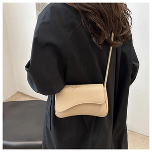 Detail of minimalist beige faux leather shoulder bag with irregular flap on black coat