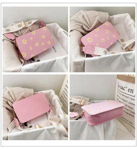 Detail view of pink crossbody bag with white daisy prints and wide floral shoulder strap