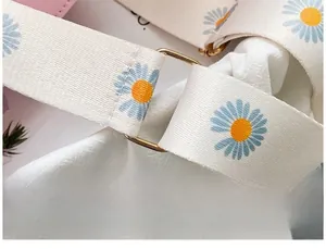 Close-up of white woven shoulder strap with blue daisy patterns and gold metal ring