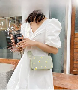 Outdoor model shot of a light green crossbody bag with daisy prints and a wide strap