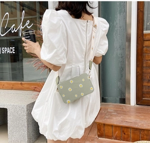Sage green crossbody bag with daisy floral prints and a wide strap shown in outdoor setting