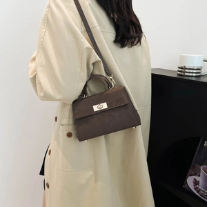 Sac à main trapèze marron foncé en cuir mat avec fermoir doré porté avec un trench-coat