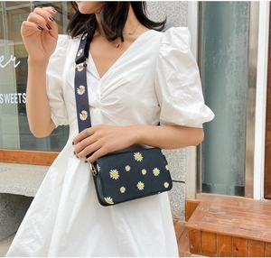 Detail of black crossbody bag with white daisy floral prints and wide shoulder strap