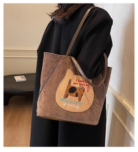 Detail of a brown corduroy tote bag featuring cat embroidery and durable leather straps