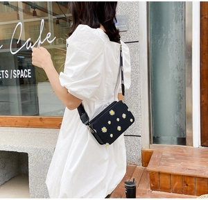 Close-up of black crossbody bag with white daisy print and wide adjustable shoulder strap
