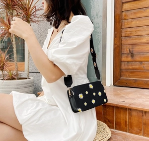 Detail of a black crossbody bag with white daisy embroidery and a wide shoulder strap