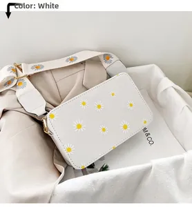 Detail of white daisy floral crossbody bag with wide shoulder strap on white cloth
