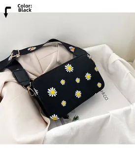 Close-up of black crossbody bag with daisy prints and golden metal hooks on white container
