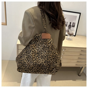 Detail of a large leopard print canvas tote bag worn by a model in a stylish interior