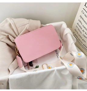 Detail of pink crossbody bag with a white daisy pattern wide strap and leather texture