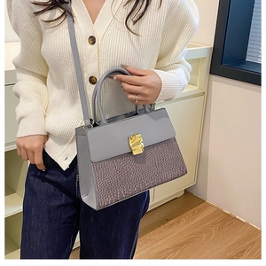 Détail d'un sac bandoulière croco mauve avec boucle dorée porté par un mannequin