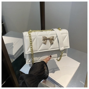 Détail d'un sac bandoulière blanc matelassé avec nœud doré et bandoulière en chaîne
