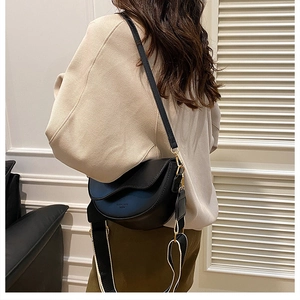 Détail du sac selle noir avec rabat ondulé et bandoulière large en tissu élégant