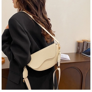 Vue latérale du sac selle crème avec bandoulière large et boucles dorées sur le mannequin