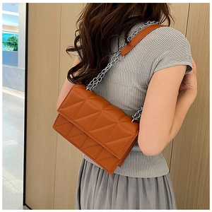 Model wearing a mustard yellow quilted shoulder bag with geometric stitching and silver chain