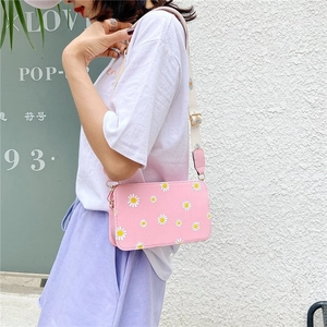 Pink crossbody bag with daisy prints and wide patterned strap shown on a model