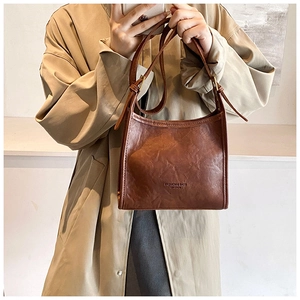 Detail of vintage brown leather shoulder bag with FASHION & BAGS lettering on beige trench coat